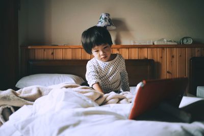 Boy watching video over digital tablet while sitting on bed at home