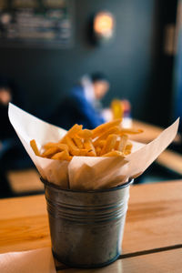 Close-up of french fries in bucket on wooden table