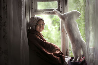 Toddler girl with a cat sitting on the window, concept of a fabulous childhood and favorite animals