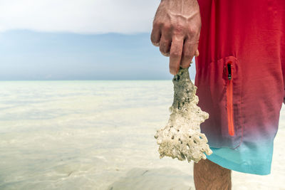 Man holding umbrella by sea against sky