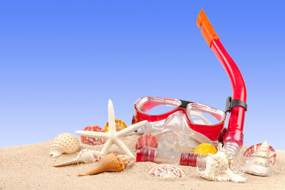 Seashells and snorkel on beach against clear blue sky