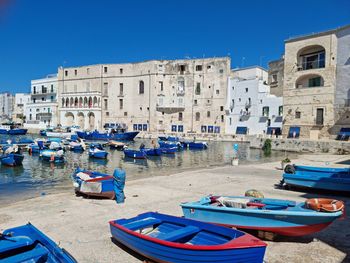 Boats moored in canal by buildings against blue sky