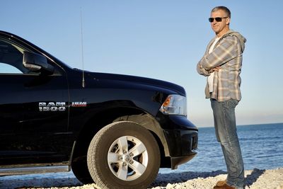 Low angle view of man standing by car against sky