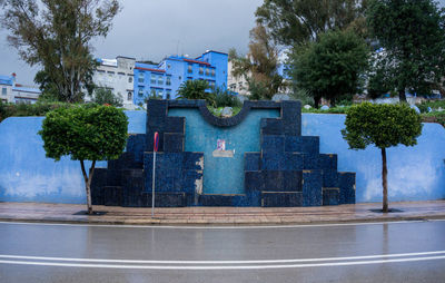 Fountain by building in city against sky