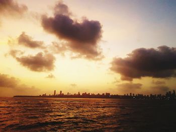 Silhouette buildings by sea against sky during sunset