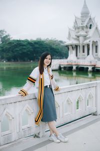 Full length portrait of young woman standing by lake