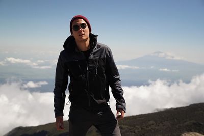 Young man wearing sunglasses standing on mountain against sky