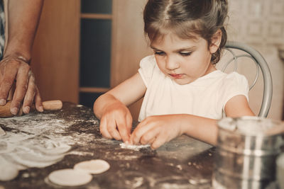 Cropped hand of father holding rolling pin preparing food with daughter