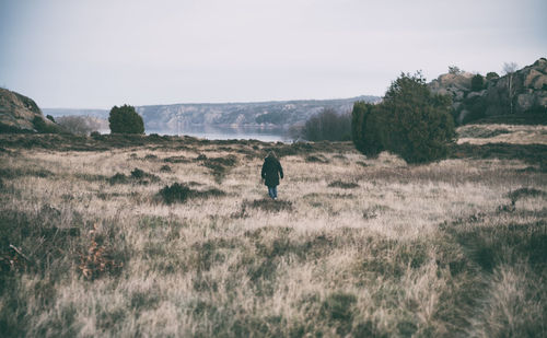 Rear view of man walking on field against sky