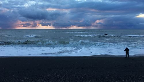 Silhouette of man on beach against dramatic sky