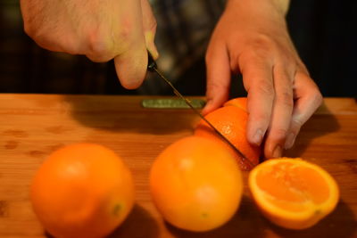 Cropped hands of man cutting orange fruits on table
