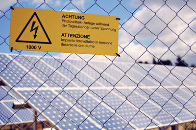Close-up of high voltage sign on fence against solar panels