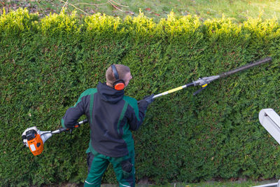 High angle view of man cutting hedge while listening to music