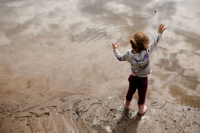 Toddler girl in rain boots throwing rock into lake in the summer