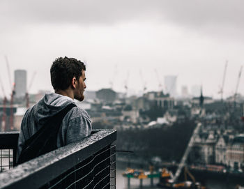 Young man looking at cityscape against sky
