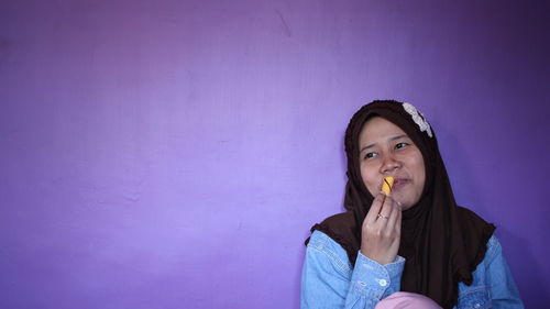 Portrait of young woman eating ice cream against wall