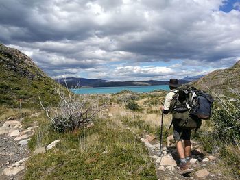 Rear view of hiker walking on field by lake pehoe against cloudy sky at torres del paine national park