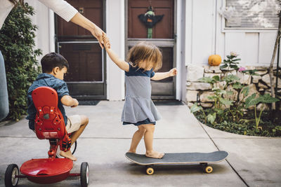 Daughter skateboarding with help of mother while son sitting on tricycle