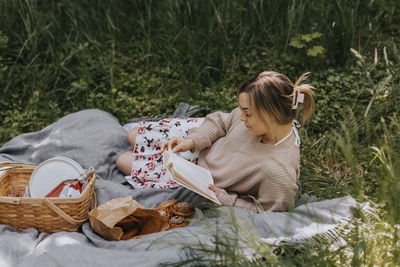 Smiling woman lying on blanket and reading book at summer day