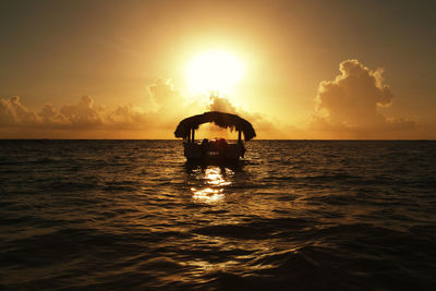 Silhouette people in sea against sky during sunset