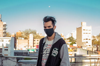 Portrait of young man with face mask in city against clear sky