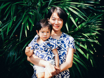Portrait of smiling mother carrying cute son while standing against plants