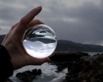 Midsection of person holding crystal ball against sky