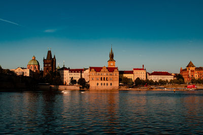 Buildings by river against clear blue sky