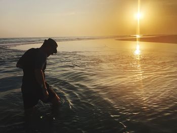 Side view of man on beach against sky during sunset