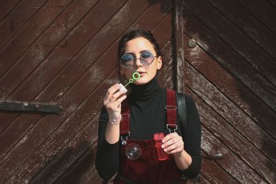 Portrait of young woman playing with bubble wand against doors