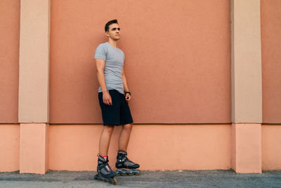 Full length of man with roller skates leaning on wall