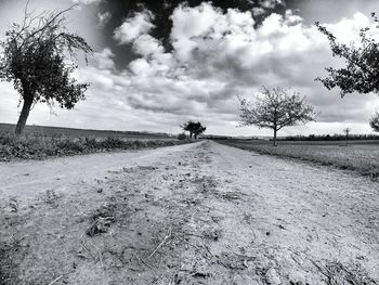 Road passing through field against cloudy sky