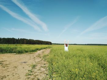 Smiling woman with arms raised standing amidst crops on field against sky