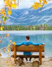 Rear view of woman sitting on bench against lake