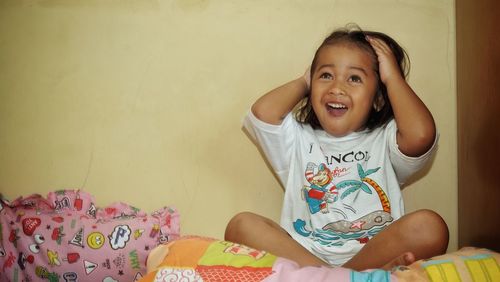 Happy girl with hand in hair sitting on bed at home