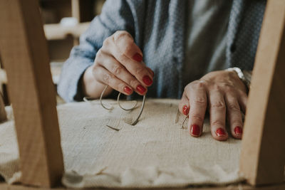 Midsection of upholsterer stitching fabric on chair in workshop