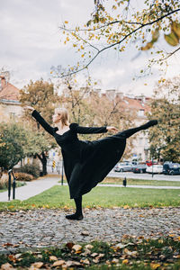 Ballerina dancing in autumn city street, modern ballet dancer in black dress, pointe shoes outdoors