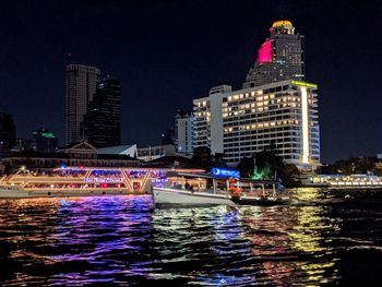 Illuminated buildings by river against sky at night