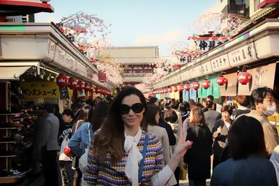 Portrait of smiling young woman showing peace sign while standing at market