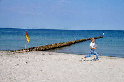 Woman standing on beach against clear blue sky