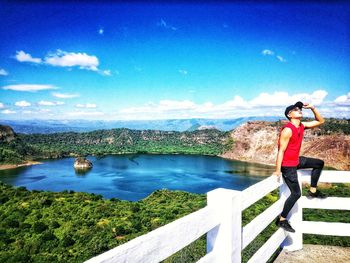 Man standing on railing by lake against sky