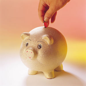 Cropped hand putting coin in piggybank over colored background