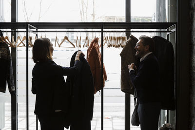 Side view of business professionals talking while hanging coats on rack in conference center