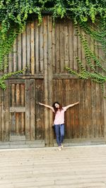 Woman with arms outstretched leaning on wooden entrance gate