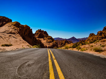 Empty road by rock formations against clear blue sky