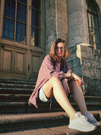 Young woman sitting on staircase against building