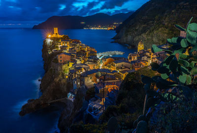 High angle view of illuminated buildings by sea against sky at dusk