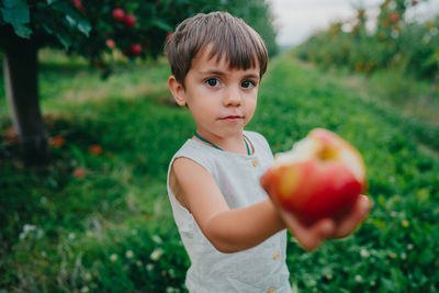 Portrait of boy holding apple against plants