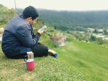 Side view of man using phone while sitting on field