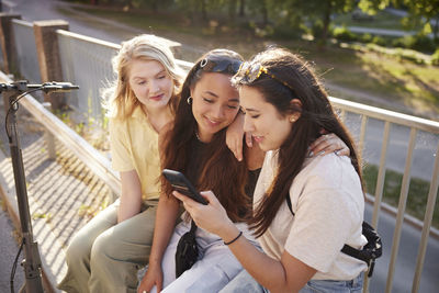 Young female friends spending time together outdoors and using phone